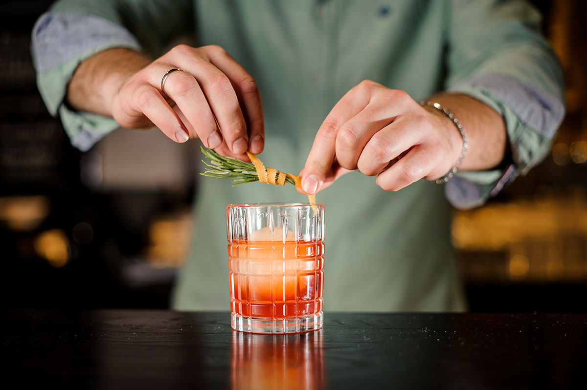 Bartender decorates cocktail with orange peel and rosemary