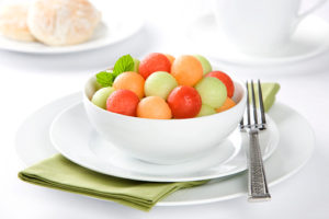 Colorful melon balls in a bowl on a white table.
