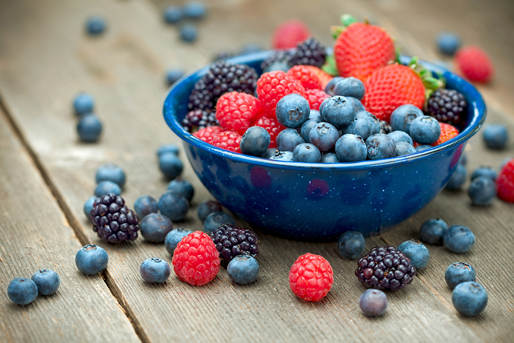 Blueberries, blackberries, raspberries, and strawberries in a bowl on a wooden table.