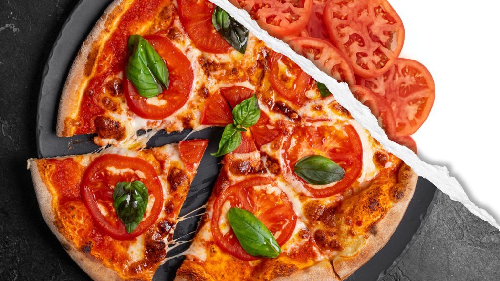 A pizza with fresh basil and tomato, featuring raw tomato slices. 